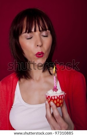 A beautiful woman is blowing out a candle on a cupcake and making a wish for her birthday. Happy Birthday.