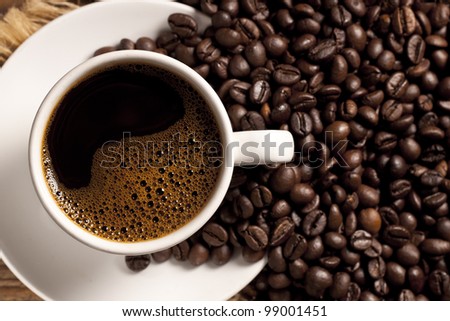 Freshly made coffee in a white cup surrounded by coffee beans on a wooden table. Fresh roasted coffee.