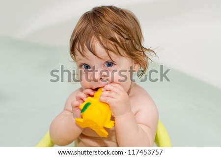 Cheery cute baby girl plays with rubber toys and smiles in a full of water bath. Portrait.