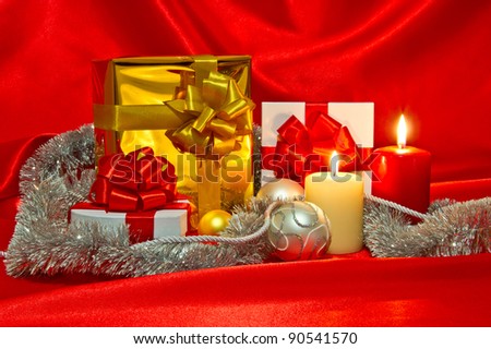 New Year (Christmas) still life with gift boxes, two candles, red satin and Christmas-tree decorations
