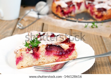 Slice of fresh plum cake with a cake in the background, horizontal