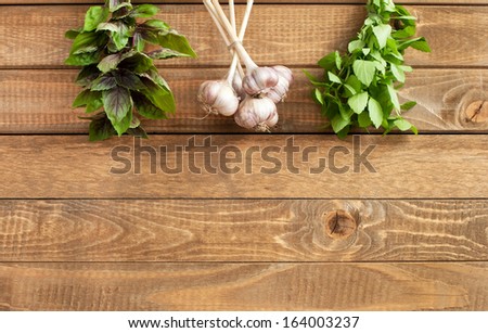 Wooden background with bunches of fresh basil and garlic and place for your text, horizontal