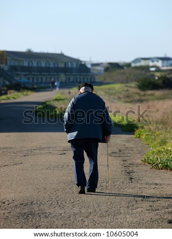 Old man with cane walking on beach front path