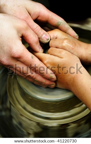 A potters hands guiding child hands to help him to work with the ceramic wheel