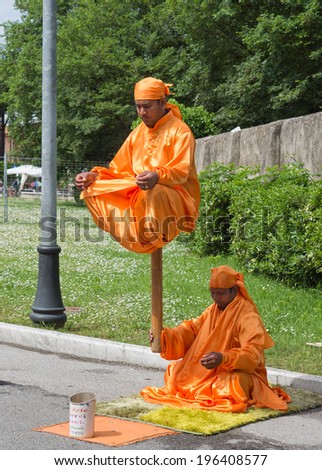 PISA, ITALY - MAY 3, 2014: Being a street artist is a strange occupation. This pair strike up an unlikely pose as monks dressed in orange robes, hoping to attract attention and money from passers-by.