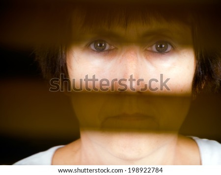 Woman face behind bars, actual or metaphor. Shadowy, indistinct figure, half hidden. Out of camera colour.e