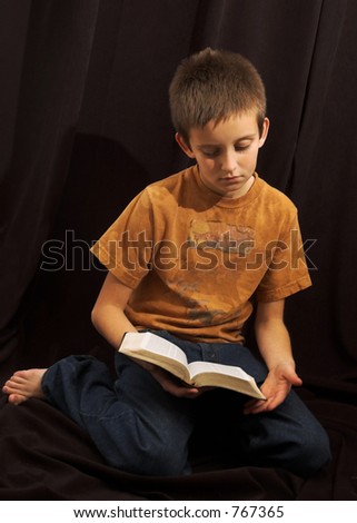young boy reading the bible, black background