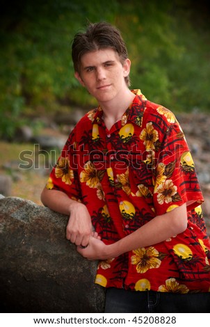 Boy in Hawaiian shirt, leaning on a rock, posing.