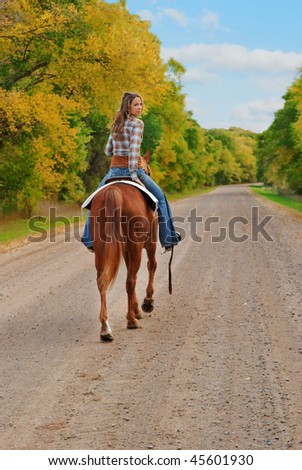 woman riding away on a horse and looking back, smiling. fall season.