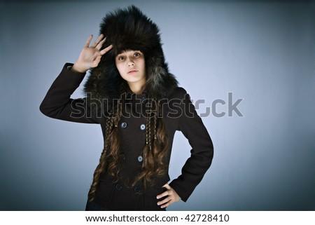 Portrait of the fabulously beautiful girl in winter fur cap on a dark background