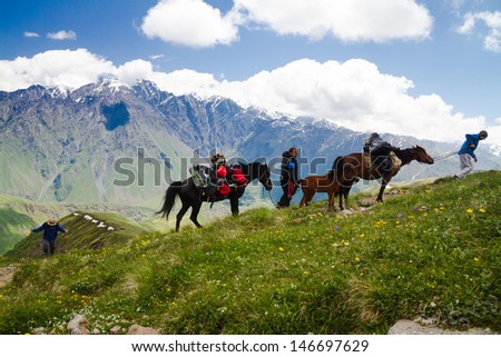 KAZBEGI, GEORGIA - JUNE 23L Men with horses carrying backpacks at Caucasus mountains on June 23, 2013 in Kazbegi, Georgia. They intend to reach Kazbek, third highest mountain in Georgia.
