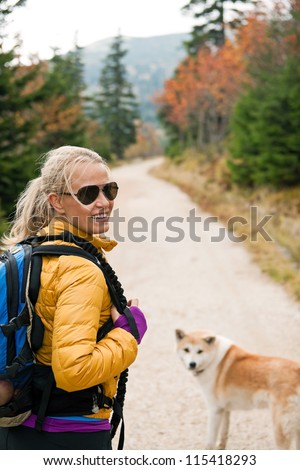 Woman hiking in mountains with akita dog, Karkonosze Mountain Range. Happy smiling hiker on autumn footpath in forest. Young female backpacker walking with canine.
