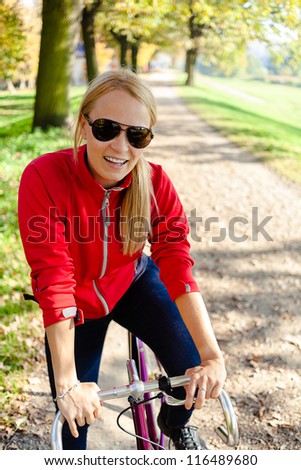 Happy woman cycling on bicycle, autumn park fitness and exercising. Recreation or commuting in city