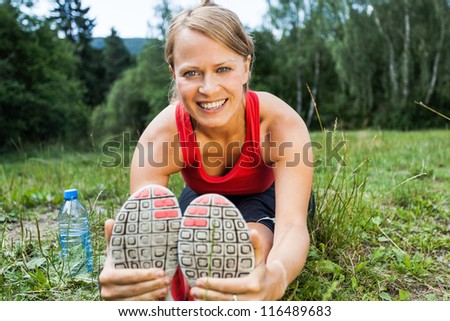 Woman runner exercising and stretching, summer nature outdoors. Female athlete working out on grass, activity and exercise