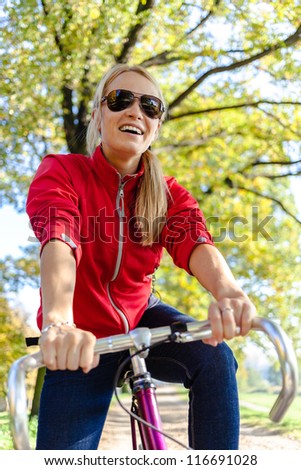 Happy woman cycling on bicycle, autumn park exercising. Young female cyclist commuting to work or relaxing in autumn nature.