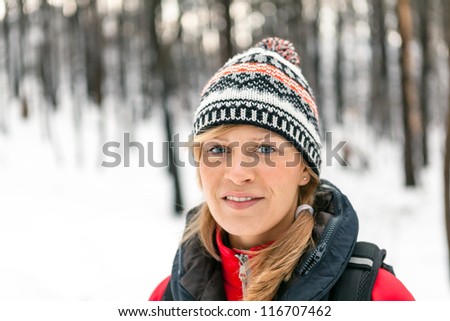 Woman hiking in white winter forest. Recreation and healthy lifestyle outdoors in nature. Beauty blond looking at camera on sunset.
