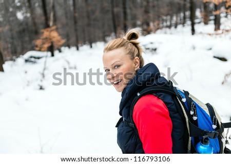 Woman hiking on snow in white winter forest. Recreation and healthy lifestyle outdoors in nature. Beauty blond looking at camera on sunset.
