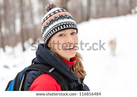 Woman hiking on snow in white winter forest. Recreation and healthy lifestyle outdoors in nature. Beauty blond looking at camera on sunset.
