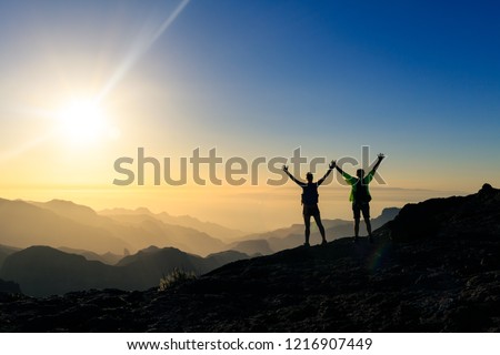 Couple hikers success and trust in mountains, accomplish with arms up outstretched. Young man and woman looking at beautiful inspirational landscape view, Gran Canaria Canary Islands.