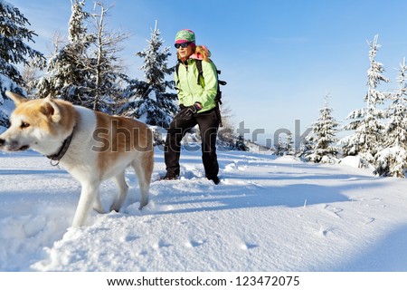Woman hiking in winter mountains with akita dog, walking on white snow. Sport and fitness in wilderness nature outdoors. Beautiful female hiker with canine.