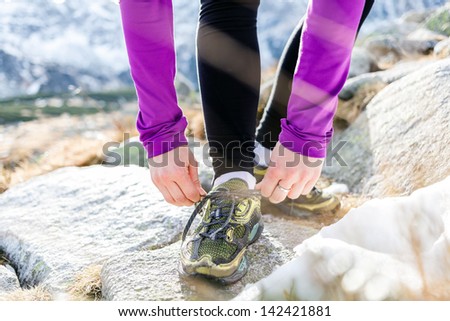Young woman running in mountains on winter fall sunny day. Motivation and inspiration fitness concept. Female runner tying sport shoe and exercising outdoors in nature, sunset.
