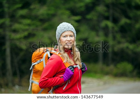 Woman hiking in forest. Recreation and healthy lifestyle outdoors in nature. Beauty blond hiker walking with backpack looking at camera.