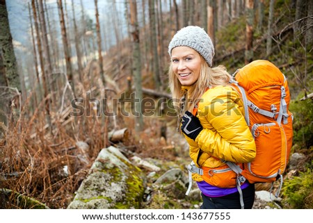 Woman hiking in autumn forest in mountains. Recreation and healthy lifestyle outdoors in nature. Beauty blond looking at camera smiling.