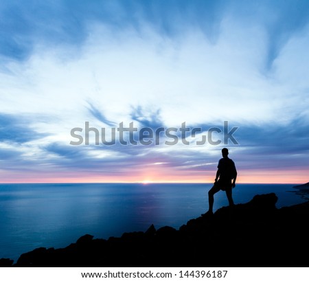 Man Hiking Silhouette In Mountains, Sunset And Ocean. Male Hiker With Backpack On Top Of Mountain Looking At Beautiful Night Landscape.