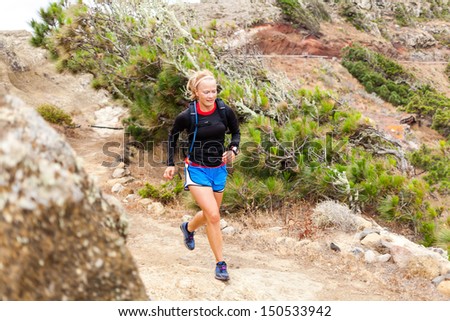 Young woman running on trail in mountains on summer day. Female runner exercising outdoors in nature on La Gomera, Canary Islands.