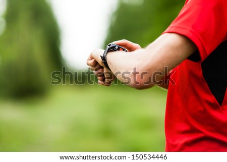 Runner on mountain trail looking at sportwatch, checking performance, heart rate pulse trace monitor or GPS position. Sport, exercising and fitness outdoors in nature.