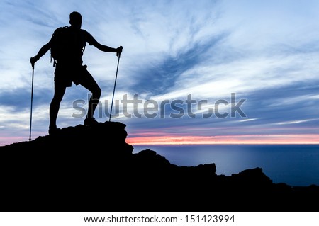 Man hiking silhouette in mountains, sunset and ocean. Male hiker with walking sticks on top of mountain looking at beautiful night landscape.