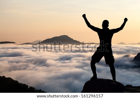 Man hiking silhouette in mountains, sunset and clouds. Male climber hiker arms outstretched on top of mountain after success climbing looking at beautiful sunset sky night landscape.