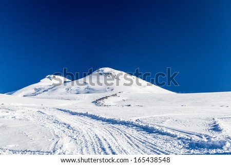 Mount Elbrus West(5642m) And East(5621), Snow Ice On Trail To The Top Caucasus Mountains Landscape In Autumn Or Winter, Russia. Beautiful Mountain Ridge Over Blue Sunny Sky.