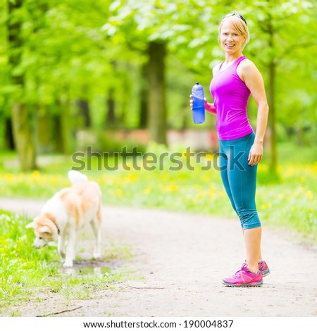 Woman runner running and walking with dog in park, summer nature, exercising in bright forest outdoors