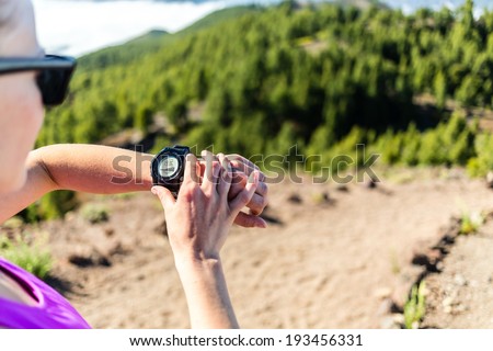 Trail runner or hiker on mountain path looking at sportwatch, checking performance or heart pulse,heart monitor. Cross country running in beautiful nature,Canary Islands. Sport and exercising outdoors