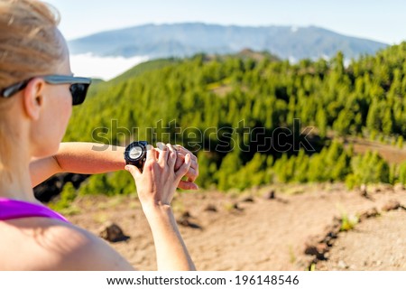 Runner on mountain trail looking at sportwatch, checking performance or heart pulse trace, heart monitor. Cross country running in beautiful nature, Canary Islands.