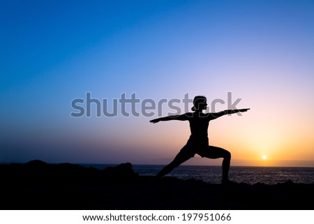 Young woman doing yoga pose warrior one, sunset silhouette in mountains. Sport and exercising in beautiful nature outdoors