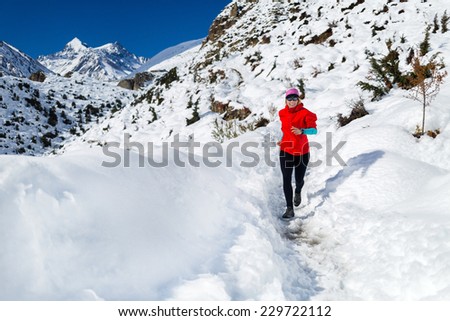 Woman running on white snow in Himalaya Mountains in Nepal. Adventure cross country runner on snow trail in beautiful mountain landscape. Motivation and inspiration fitness activity.