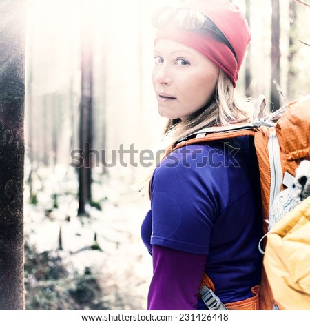 Woman hiking in white winter vintage forest, backlight by morning sunlight rays, recreation and healthy lifestyle outdoors in nature. Beauty blond retro hiker backpacker looking at camera on sunset.