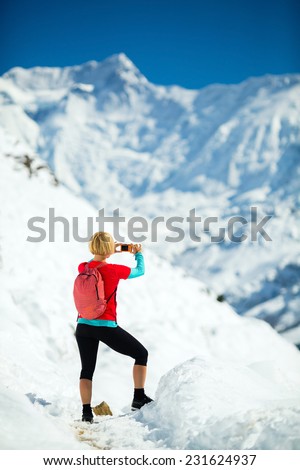 Young happy woman hiker taking photos on mountain peak summit in winter mountains. Climbing inspiration and motivation, beautiful landscape. Fitness healthy outdoors activity in Himalayas, Nepal