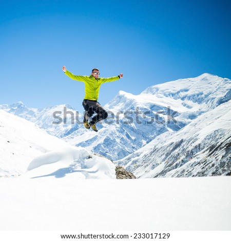 Happy young male hiker jumping in white winter mountains Himalayas, inspirational landscape.  Success climber climbing on snow, beautiful landscape with Annapurna peak in background