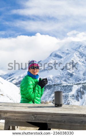 Young woman hiker drink coffee or tea in beautiful Himalaya mountains on hiking trip base camp Nepal. Active person resting outdoors in winter white nature. Female backpacker camping recreation active