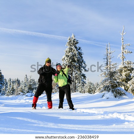 Happy man and woman hikers trekking on snow trail in winter mountains. Young couple on white and cold vacations in winter forest, beautiful natural landscape.