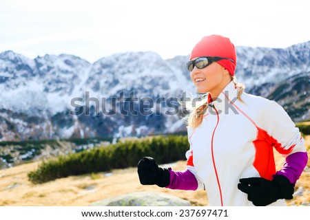 Young woman running in mountains on winter or fall sunny day. Happy beautiful female runner exercising outdoors in nature, using black sunglasses for sunset. Healthy lifestyle outside adventure.