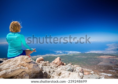 Young woman doing yoga meditation outside natural beautiful inspirational landscape environment, fitness and exercising motivation and inspiration in sunny mountains over blue sky and ocean sea.