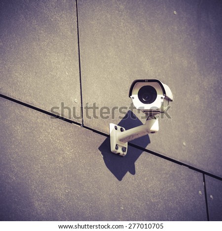 White security camera on gray office building, safety surveillance system outside looking around in city urban scene, cctv electronics industry concept