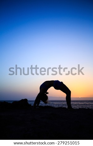 Young woman stretches yoga bridge pose, sunset silhouette in mountains. Motivation inspiration, sport and fitness stretching exercising outdoors in nature.