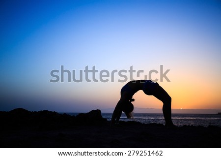 Young woman stretches yoga bridge pose, sunset silhouette in mountains. Motivation inspiration, sport and fitness stretching exercising outdoors in nature.