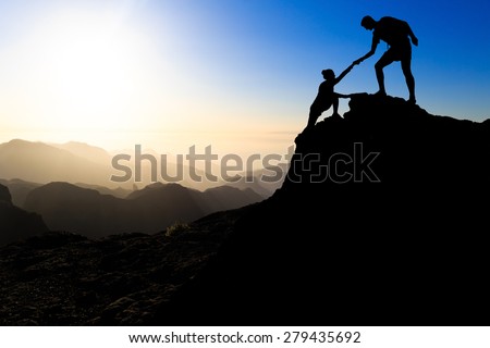 Teamwork couple hiking help each other trust assistance silhouette in mountains, sunset. Team of climbers man and woman hiker helping each other on top of mountain, climbing trust beautiful landscape.