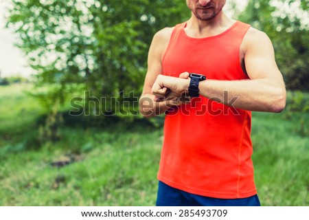Runner on mountain forest trail checking looking at sport watch smart watch, cross country runner checking performance GPS position or heart rate pulse. Sport equipment in use outdoors on summer trail